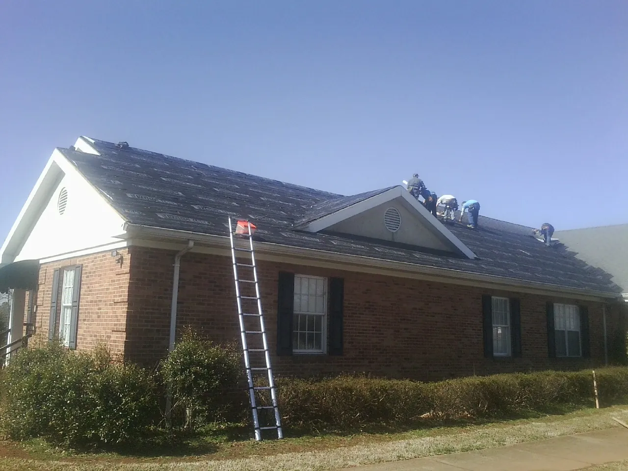 Crew tearing shingles off a brick ranch roof with a ladder set — Metal Roof Repair work by our crew in Hayes