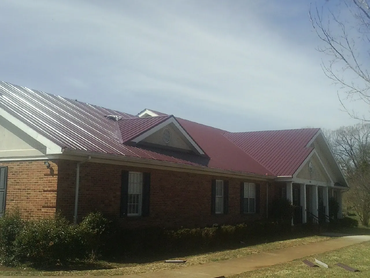 Red metal roof with gabled entries on a long brick building, from a Hail Damage Roof Repair job in Hayes