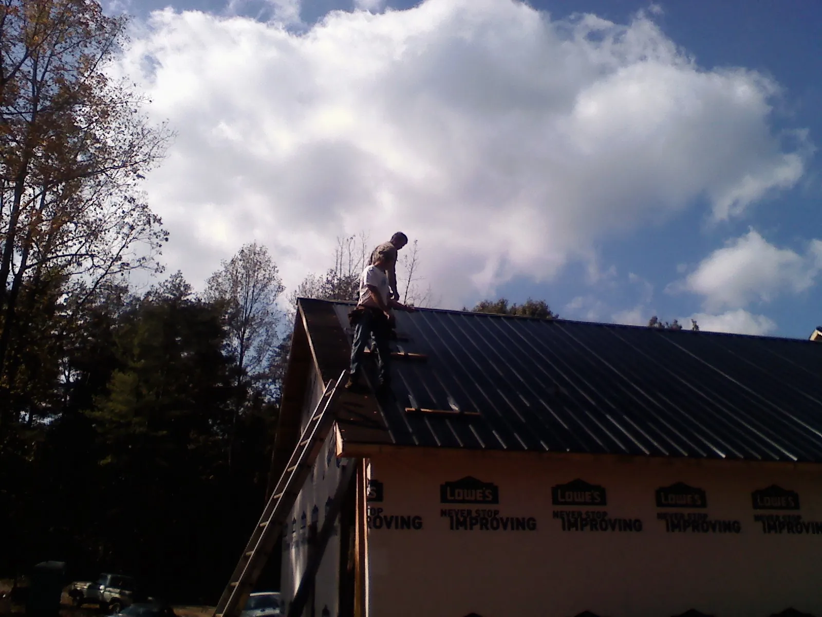 Roofer fastening dark metal panels high against a cloudy sky, from a Roof Inspection job in Hayes