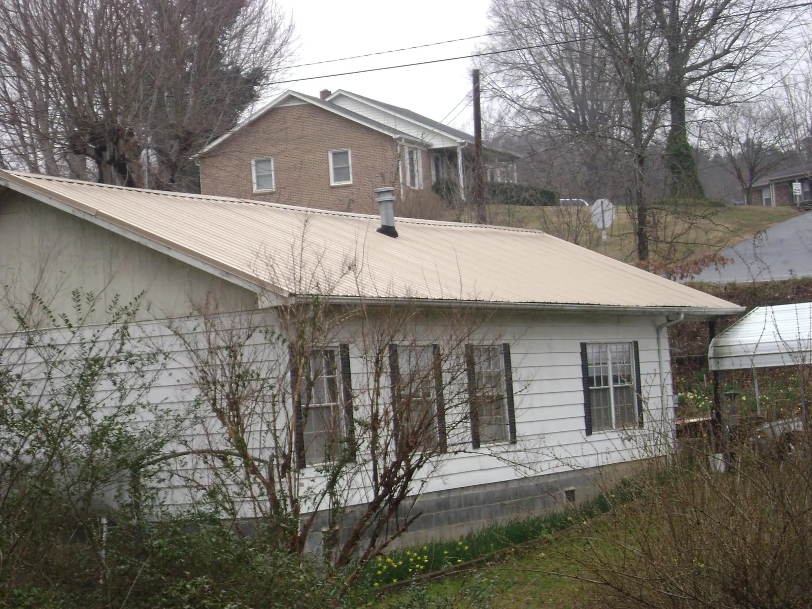 Tan metal roof on a white sided house set into a hillside — Commercial Roofing by Roofing Brothers in Hayes