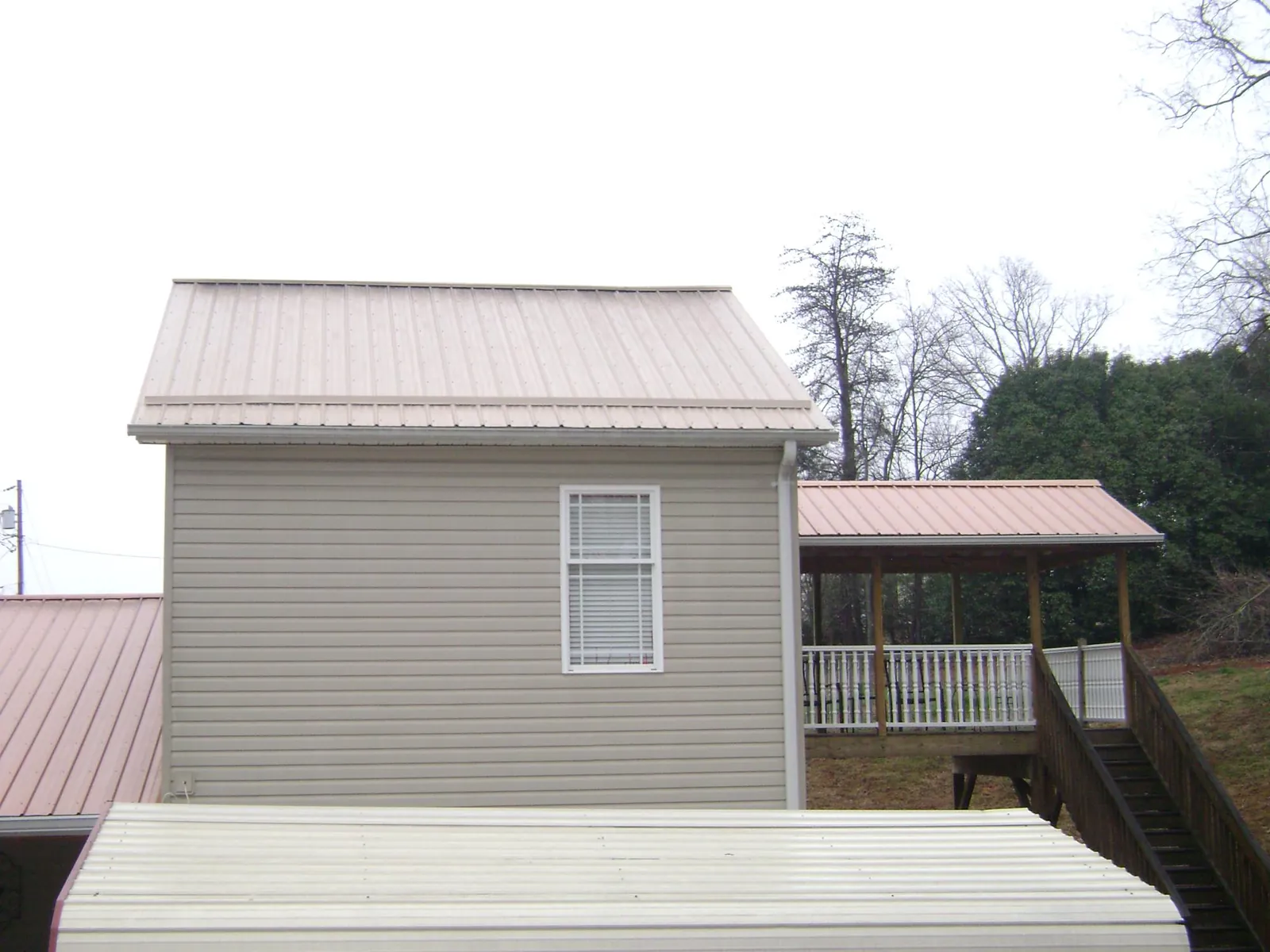 Tan metal roofs on a two story addition and attached porch, from a Roof Replacement job in Hayes